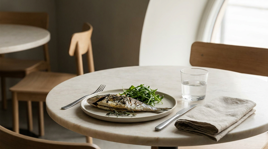 Gedeck auf hellem Marmortisch mit gegrilltem Fisch, grünem Salat, Besteck und einem Glas Wasser