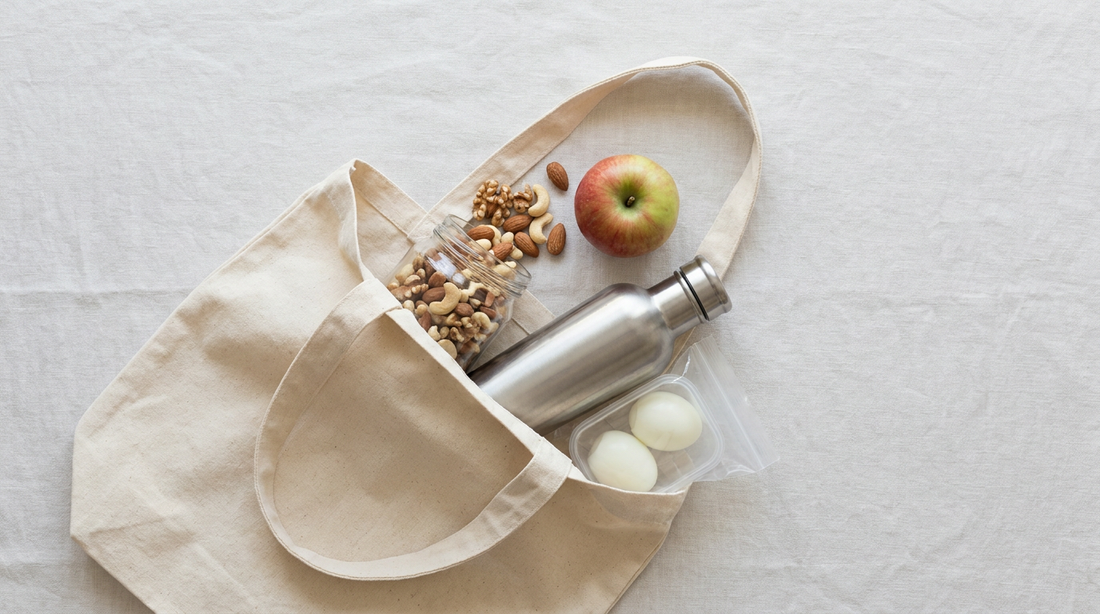 Offene Stofftasche von oben mit Nussglas, Apfel, Edelstahl-Shaker und Dose mit gekochten Eiern