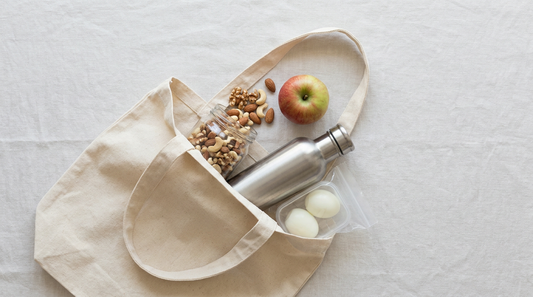 Offene Stofftasche von oben mit Nussglas, Apfel, Edelstahl-Shaker und Dose mit gekochten Eiern